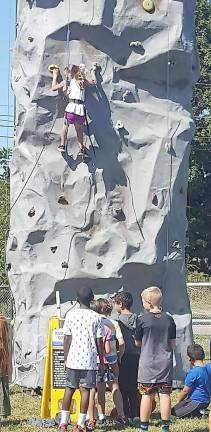 Children watch a girl as she climbs the wall and patiently wait their turn to climb