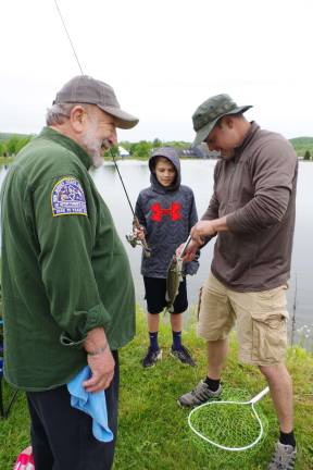 New Jersey State Federation of Sportsmen&#xfe;&#xc4;&#xf4;s Clubs member Jim Cosmano laughs as Damon Arapkiles helps his son Nicholas, 11, with a 12-inch small-mouth bass. They are all from Andover Township.