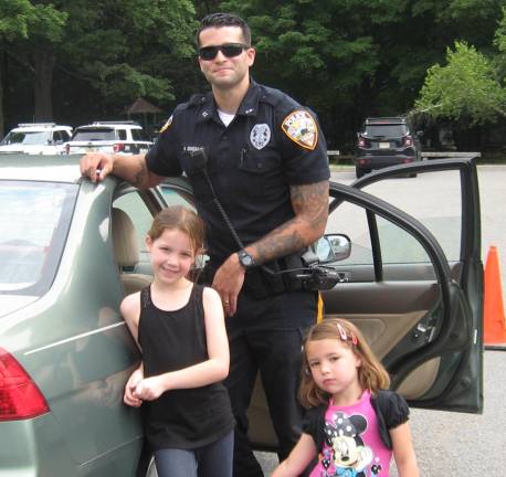 Vernon Officer Gonzalez poses with Alex and Annie Wieladek as he checks the girls' family car for safety seats.