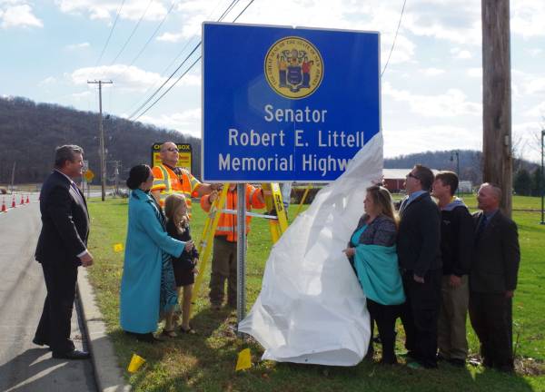 New Jersey DOT workers are shown unveiling the &#xfe;&#xc4;&#xfa;Senator Robert E. Littell Memorial Highway&#xfe;&#xc4;&#xf9; as the bill&#xfe;&#xc4;&#xf4;s sponsors and members of the Littell family watch the unveiling.