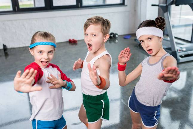Gym teacher uses CrossFit to help with life lessons Group of little kids in sportswear exercising and posing at camera in gym children sport school concept