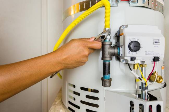 Plumber installing a gas line on a newly installed water heater tank. Great concept for plumbing, water heater repair, installation &amp; maintenance for your next project.