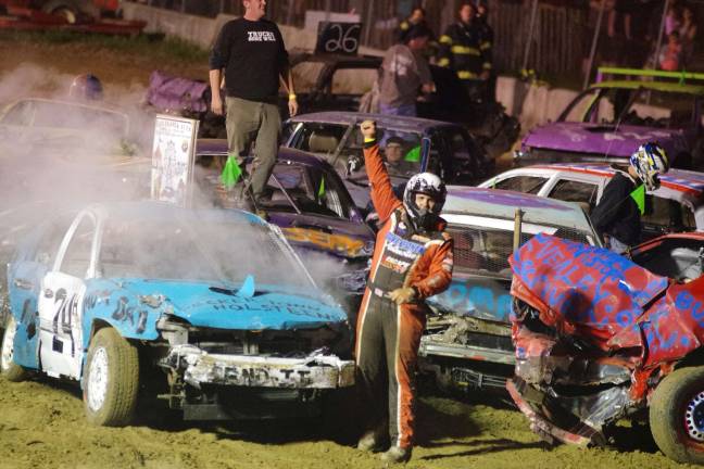 Cars bounce around at demolition derby Standing next to his car (24) Billy "Trucker" Hotalen of Wantage, New Jersey raises his fist in triumph after winning the compact car heat.
