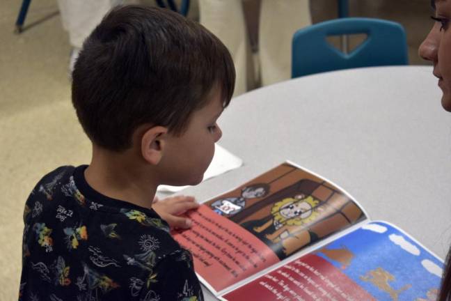 Preschool student Rory Coombs looks at the book that high school students created for him and his classmates.