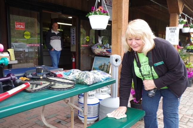 Vernon Township Woman's Club member Maria Dorsey dries off a bench so that visitors can rest during their shopping trip.