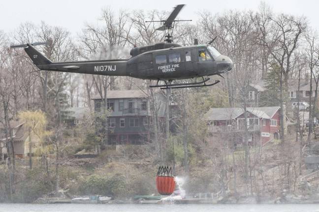 A state forest fire helicopter drops down over Highland Lakes to pick up a bucket of water and heads back to the fire scene in Vernon at 12:00 PM on Tuesday.