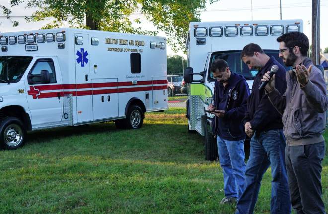 PHOTOS BY VERA OLINSKI From right, Pastor Micah Coleman Campbell blesses the two new ambulances, as squad members James Perrier and Albie Garcia listen.