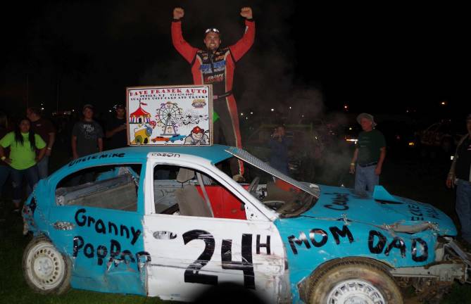 Cars bounce around at demolition derby Standing on his car (24) Billy "Trucker" Hotalen of Wantage, New Jersey raises his fists in triumph after winning the compact car heat.