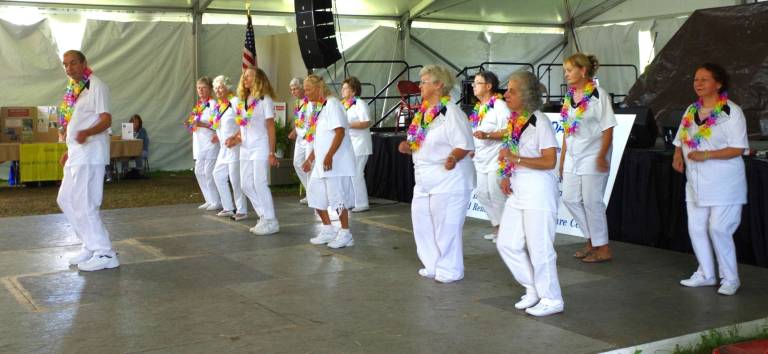 Led by David Cross, the Sparta Recreation Dancers and Bristol Glen Dancers are shown performing before a packed audience on the stage in the performing arts tent.