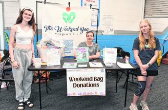 Jenna Gilmartin, Kelly Hermand and Abigail Hanson of The Weekend Bag Program stand in front of the table.