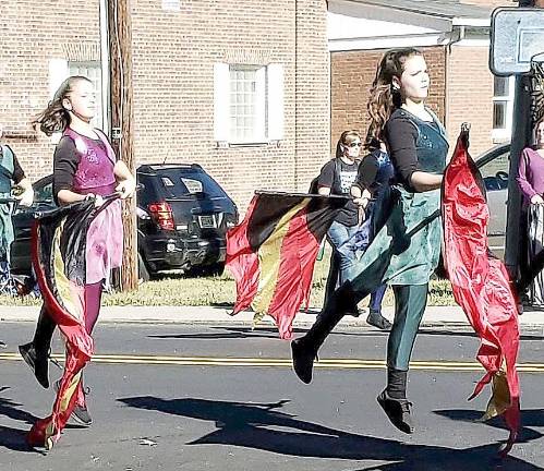 Parade performers leap together as flags are waved.