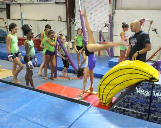 At far right instructor Tim Rajkumar and gymnasts watch as a hand stand is executed.