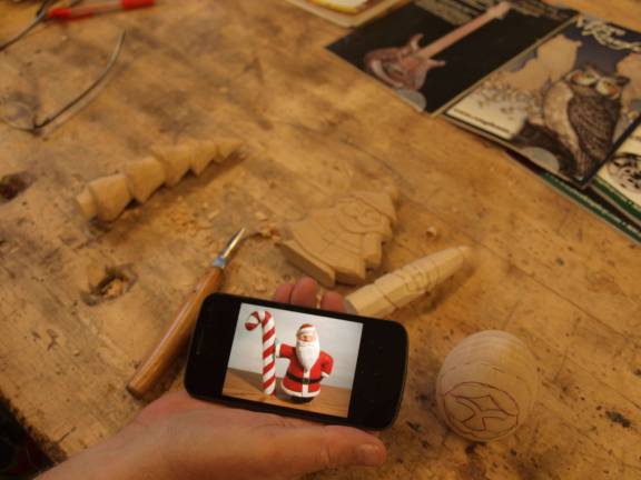 Ken Dispoto of Sussex with his carved creations on a table and a cellphone picturing a finished product.