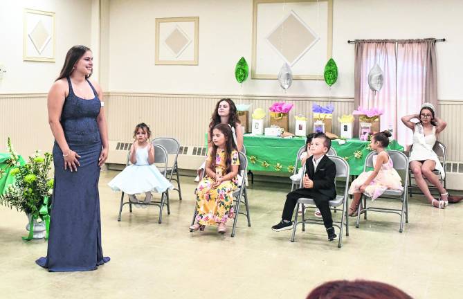 Miss Ogdensburg 2026 Fiona stands as little Miss Ogdensburg Elena, Mister Ogdensburg Brody and Little Miss Ogdensburg Elena sits.