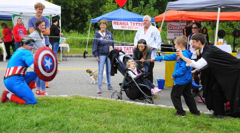 On right, Cole Benkendorf - Harry Potter - shoots silly string at Captain America - Nathan Fitch - on left, while a little boy plays with Potter's wand.