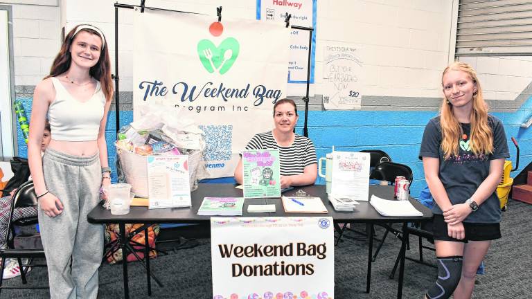 Jenna Gilmartin, Kelly Hermand and Abigail Hanson of The Weekend Bag Program stand in front of the table.